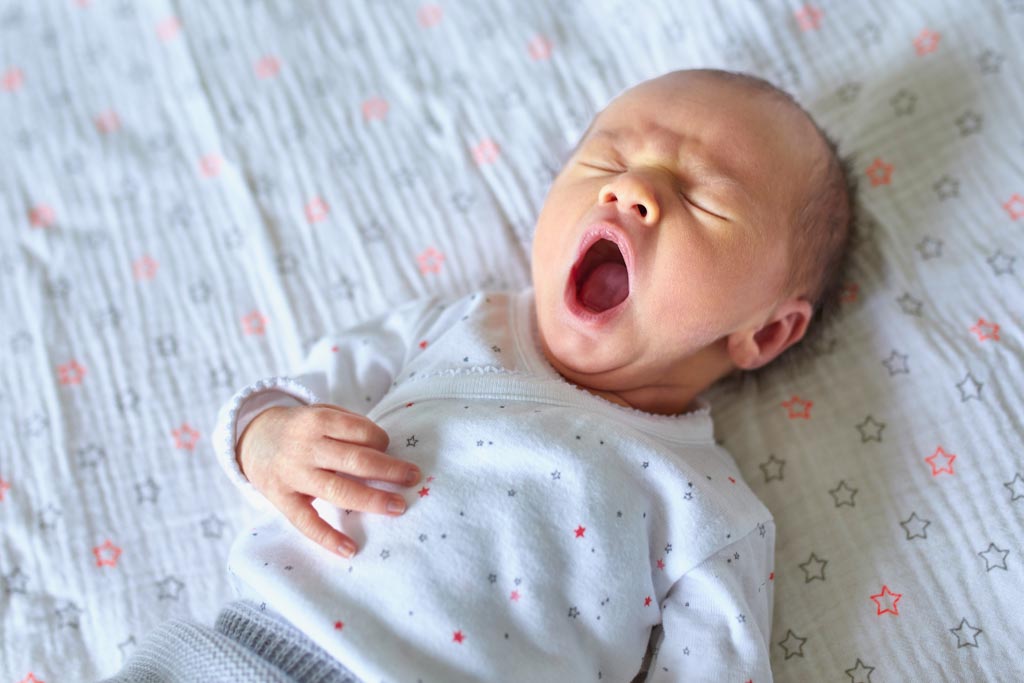 Newborn baby yawning while resting on a white blanket with star pattern